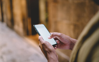 Cropped image on male holding mobile phone with mock up screen sending text messages and mails, man using smartphone for online communication and chatting via 4G internet connection on street