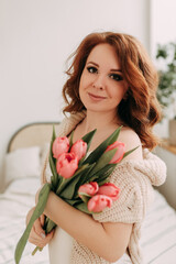 A close up portrait of a beautiful delicate sensual elegant red haired young woman holding and smelling a bouquet of spring flowers tulips enjoying the fragrance celebrating the holiday of March 8