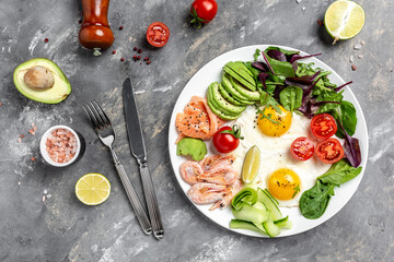 keto diet food. breakfast with salmon, boiled shrimps, prawns, fried eggs, fresh salad, tomatoes, cucumbers, and avocado. Concept of healthy eating. top view