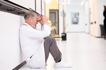 Tensed doctor sits alone on floor in corridor of hospital - Powered by Adobe