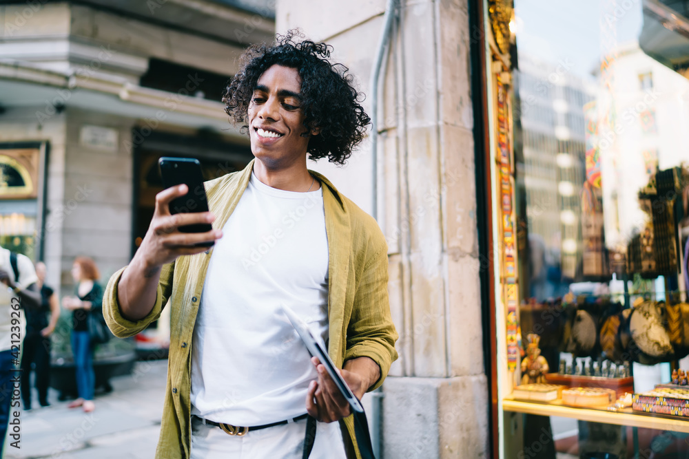 Poster cheerful young male with curly hair using mobile phone for sending messages and text email, smiling 