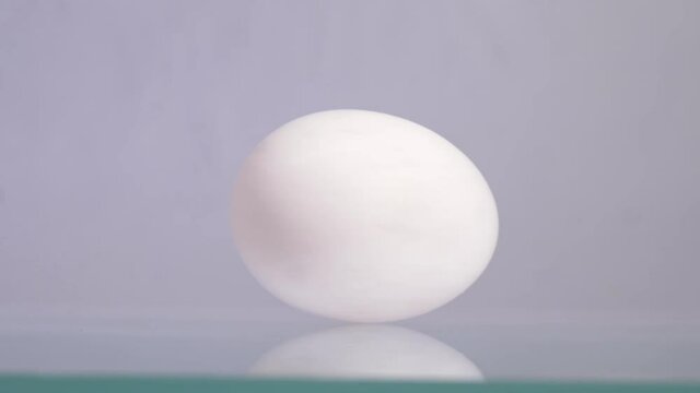 Happy Easter. White chicken egg spinning and rolling on a white background with beautiful reflection