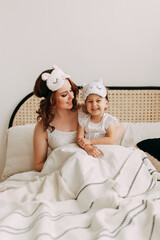 Obraz na płótnie Canvas Happy family sleepy funny cute beautiful mom and daughter small child relaxing lying on the bed Playing spending time together in a cozy bright bedroom at home, mother's day, selective focus