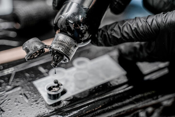 Close-up photo of tattoo master in black gloves pouring inks into plastic cup.