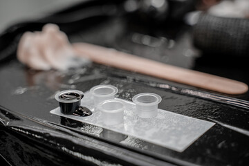 Close-up photo of tattoo master in black gloves pouring inks into plastic cup