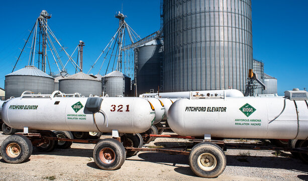 Illinois, USA, October 2021 - Rows of white ammonia tanks on wheels with large corn grain bins in background. warning decals, stickers, agriculture, food, anhydrous, fertilizer, chemical, 
