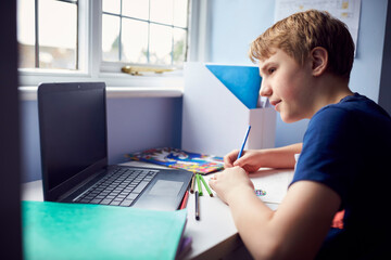 Boy Sitting At Desk Home-Schooling Using Laptop For Online Learning During Health Pandemic - obrazy, fototapety, plakaty