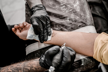 Hand of professional artist wiping finished tattoo with hygienic napkin, close up view.