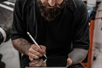 Close-up young man tattoo artist with beard drawing pencil and sketch standing in workshop place.