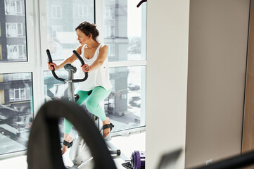 Young woman doing morning cardio workout exercising on stationary bike