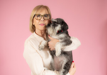 Senior woman holding her schnauzer puppy over pink background.