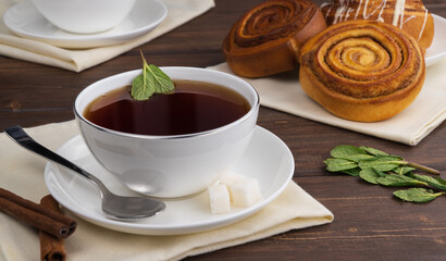 hot black tea with mint leaves in a white mug on a wooden table. selective focus. morning tea ceremony. aromatic drink with sugar and mint. delicious cinnamon rolls for breakfast. meal concept