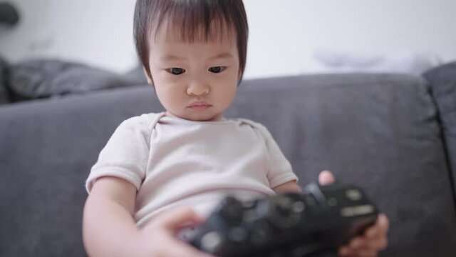 Portrait facial focus on little cute baby girl intently looking at camera's screen, adorable infant randomly pressing button and sitting in front of living room's sofa, imagination playing