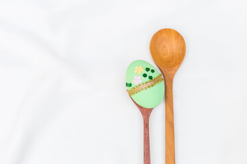 Green easter egg on wooden spoon with space on white fabric texture background