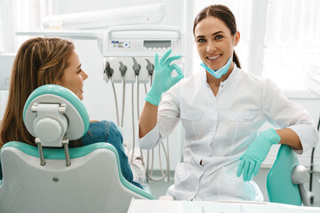 European mid dentist woman showing ok sign while working with patient
