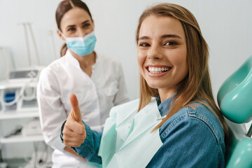 European young woman showing thumb up while sitting in medical chair