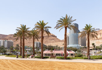 View of the beach on the Ein Bokek embankment on the coast of the Dead Sea, tourist hotels and sandy mountains in the background, in Israel