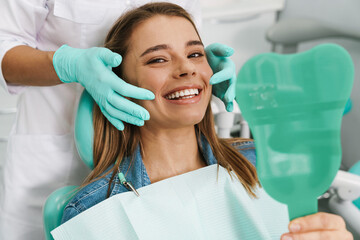 European young woman smiling while looking at mirror in dental clinic