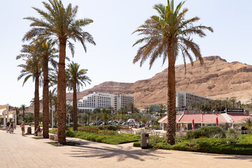 View of the beach on the Ein Bokek embankment on the coast of the Dead Sea, tourist hotels and sandy mountains in the background, in Israel