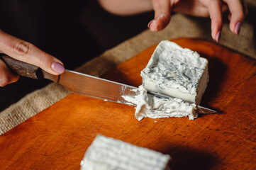 Valencay cheese on a wooden board. Cheesemaker cuts cheese with blue mold, close-up. French soft cheese from goat's milk. Cheese composition