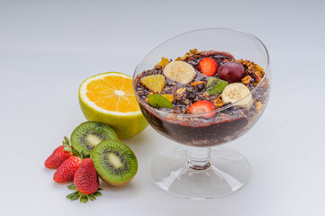 Acai with granola and fruits like strawberry, grape, banana, papaya, orange, kiwi in a glass bowl on a white background. Healthy food.