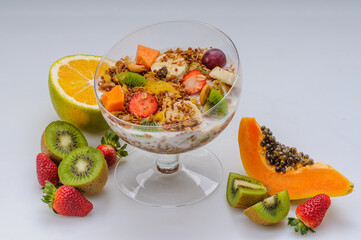Yogurt with granola and fruits like strawberry, grape, banana, papaya, orange, kiwi in a glass bowl on a white background. Healthy food.