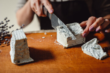 Fototapeta na wymiar Cheesemaker cuts french soft cheese with blue mold, closeup. A piece of Valencay cheese on a knife.