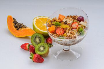 Yogurt with granola and fruits like strawberry, grape, banana, papaya, orange, kiwi in a glass bowl on a white background. Healthy food.
