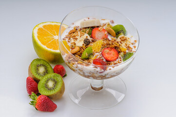 Yogurt with granola and fruits like strawberry, grape, banana, papaya, orange, kiwi in a glass bowl on a white background. Healthy food.