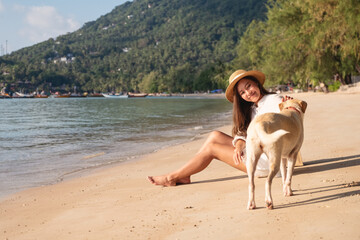 A beautiful young asian woman calling and playing with a dog on the beach