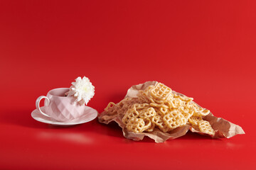 a flower and cookies on a red background with a pink cup on a saucer 