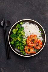 Teriyaki shrimp, rice and broccoli on a black plate. Asian healthy food. Seafood with garnish