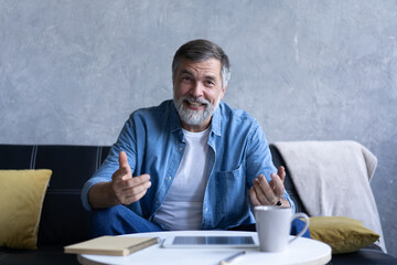 Happy senior retired man blogger looking at camera recording vlog, webcamera view portrait