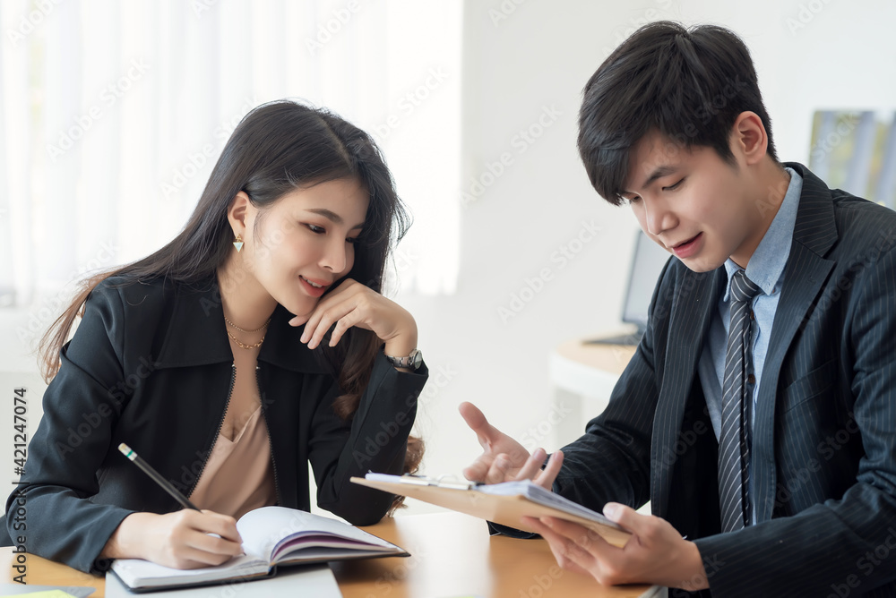 Poster two young asian business people explaining a list of collaboration using document and taking notes a