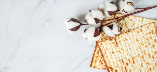 Happy Passover. Background religious Jewish holiday Pesach. Matzo bread and cotton flowers on a white marble. Copy space.