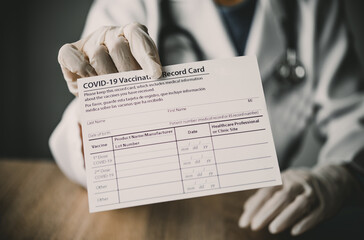 Coronavirus vaccination record card in the hands of a doctor to a patient who has already been...