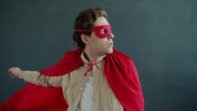 Slow motion of funny guy super hero wearing red cape and mask looking around then running away. Super heros and heroic achievements concept.