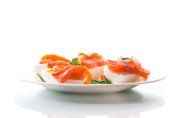 halves of boiled eggs with pieces of salted salmon on white background