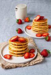 Stack of pancakes with strawberry and pouring golden honey on grey background 
