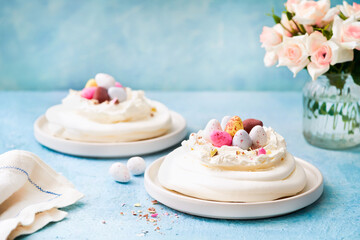 Meringue nest cake with colorful chocolate eggs, buttercream frosting on light blue background with copy space. Selective focus. Food ideas for kids. Easter cake. Spring love feast concept. Close up.