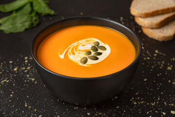 Vegetarian homemade pumpkin and carrot soup with cream and pumpkin seeds on dark background close up