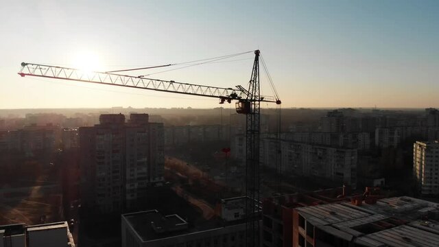 Drone shot of a crane boom or boom at a construction site during sunset. Close-up view of a boom crane lifting heavy materials at a construction site in northern Europe. Crane operator in the cockpit