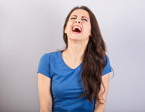 Beautiful positive excited laughting woman with wide opened mouth in blue shirt and long hair on blue background. Closeup
