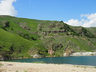 white clouds cover the tops of the rocky mountains. near the pond with clear mountain clear water and mountains with Alpine meadows