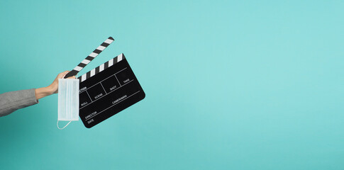 Hands with grey suit and hold black Clapper board or movie slate with face mask. it use in video production ,movies and cinema industry on blue and green or mint background.