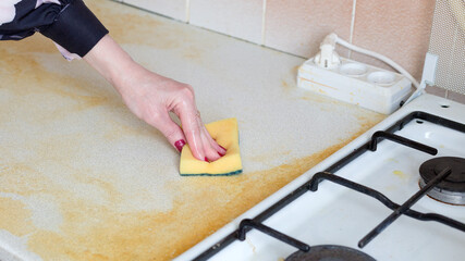 Woman wiping dirty yellow greasy table and gas stove.,