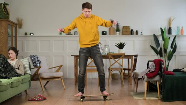 Young funny man at home learning to stand on a skateboard from video lessons and falls