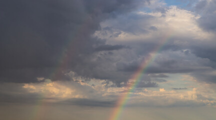Fototapeta na wymiar rainbow on dramatic dark sky with rays and white clouds