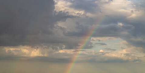 Fototapeta na wymiar rainbow on dramatic dark sky with rays and white clouds