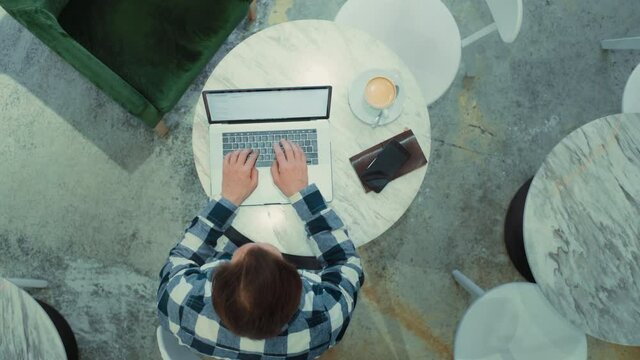 Top View On Middle Aged Adult Man Sitting At Cafe, Working On Laptop, Remotely From Outside The Office. Zoom Out Shot Of Freelancer Working. Work From Home Or From Coworking Modern Space